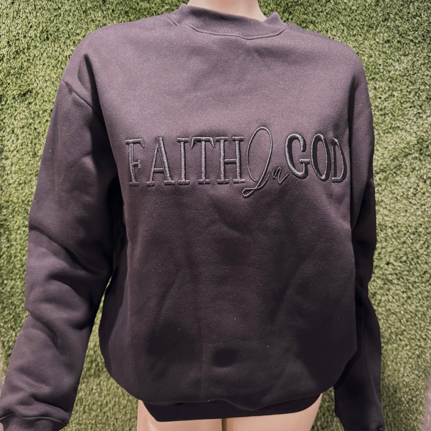A black sweatshirt with 'FAITH IN GOD' embroidered on the chest.