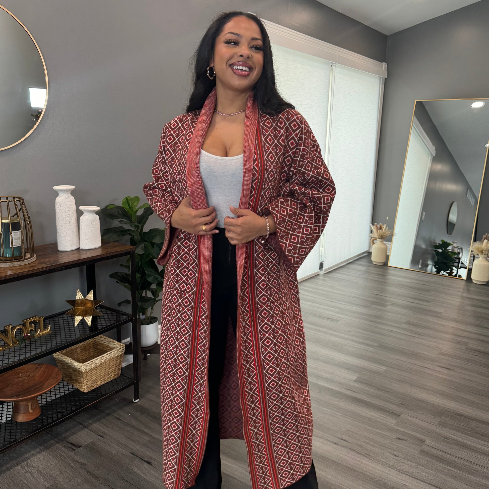 A person wearing a brown knit cardigan with a geometric pattern, standing in a room with light decor.