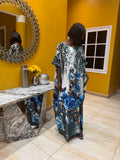 Woman in a floral kaftan dress standing in front of a yellow wall with a mirror.