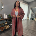 A person wearing a brown knit cardigan with a geometric pattern, standing in a room with light decor.